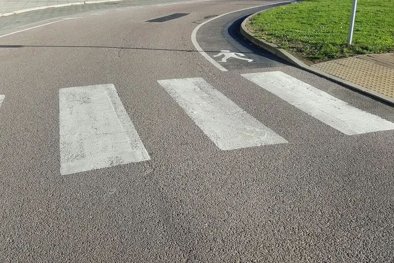 Un passage piéton blanc sur l’asphalte, au bord d’un virage