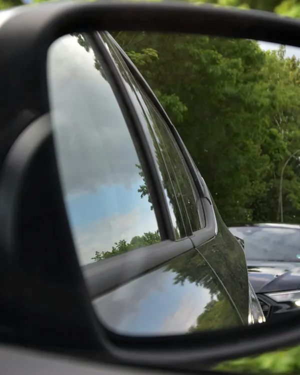 Un rétroviseur de voiture où se reflètent des arbres et la file derrière